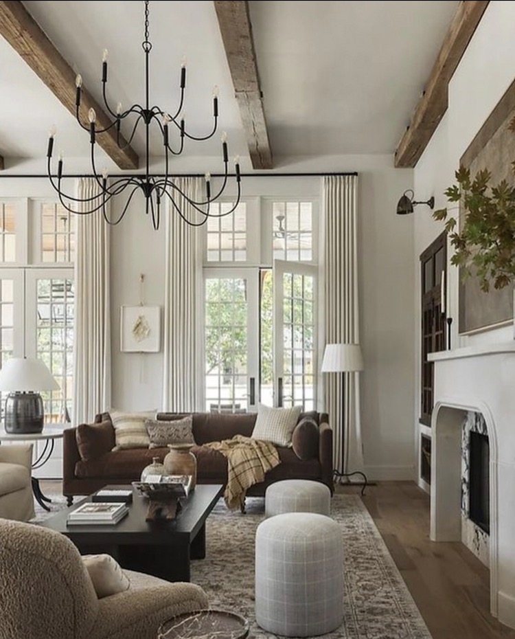 Neutral living room with brown sofa, fireplace, black coffee table, soft rug, and tall curtains showing how to arrange living room furniture with a fireplace.